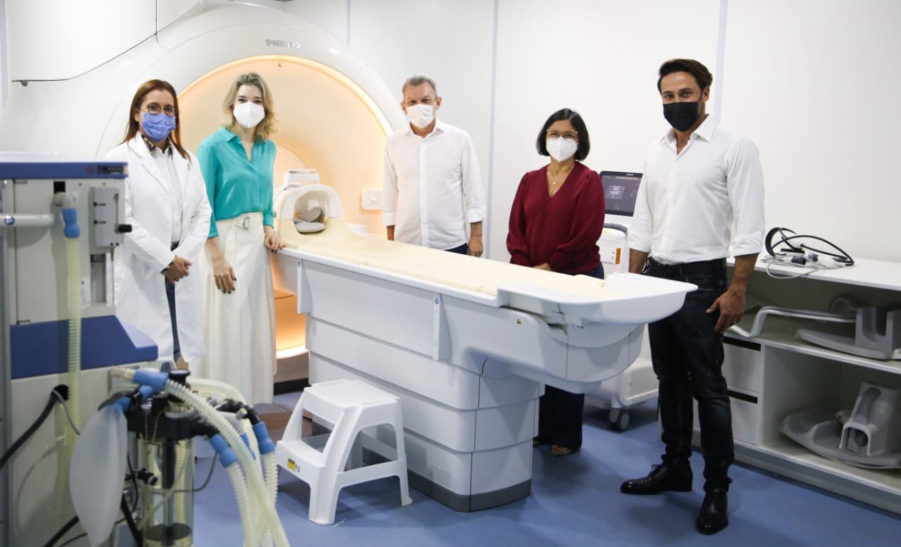 um grupo de pessoas com máscara dentro de uma sala onde há um aparelho de ressonância magnética
